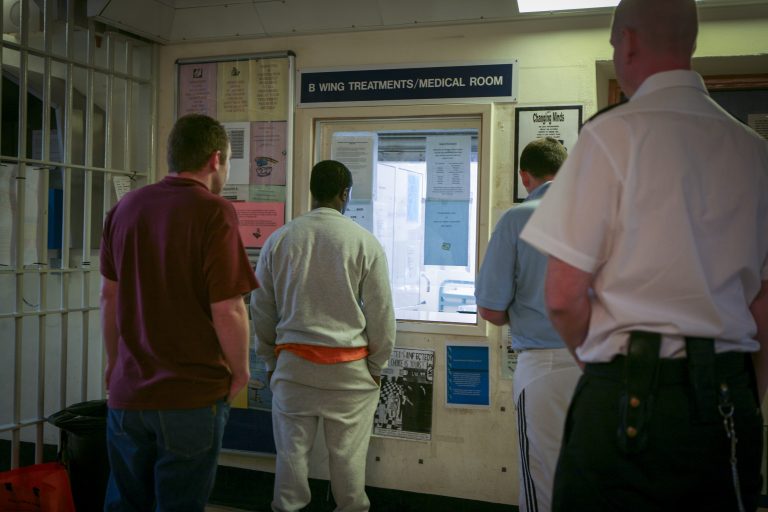 A prison officer watches men as they collect their medication from the B wing treatment room at Wandsworth prison.